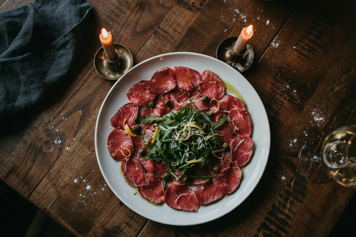 Carpaccio od goveđeg filea sa rukolom, parmezanom i kaparima na belom tanjiru